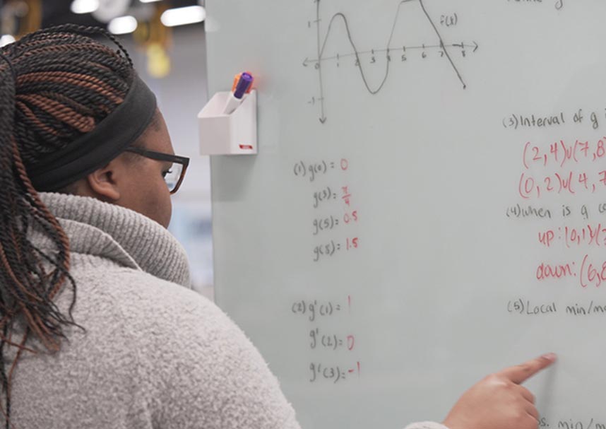 A student writing engineering homework on a whiteboard
